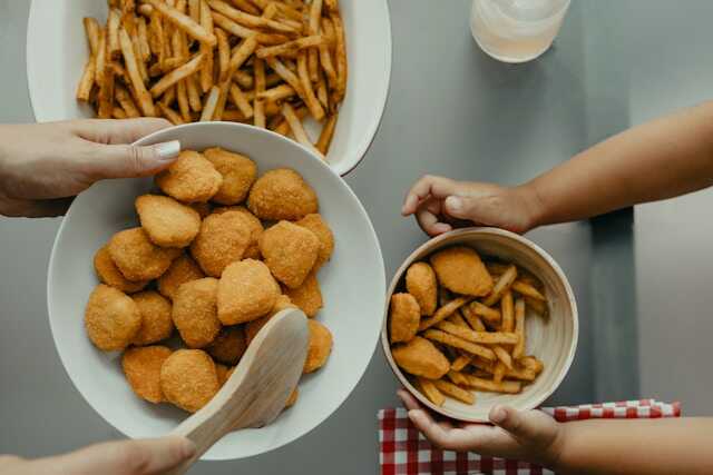 Panirani-proizvodi-chicken-nuggets-i-pomfrit-u-belim-činijama-koje-drže-ljudi.